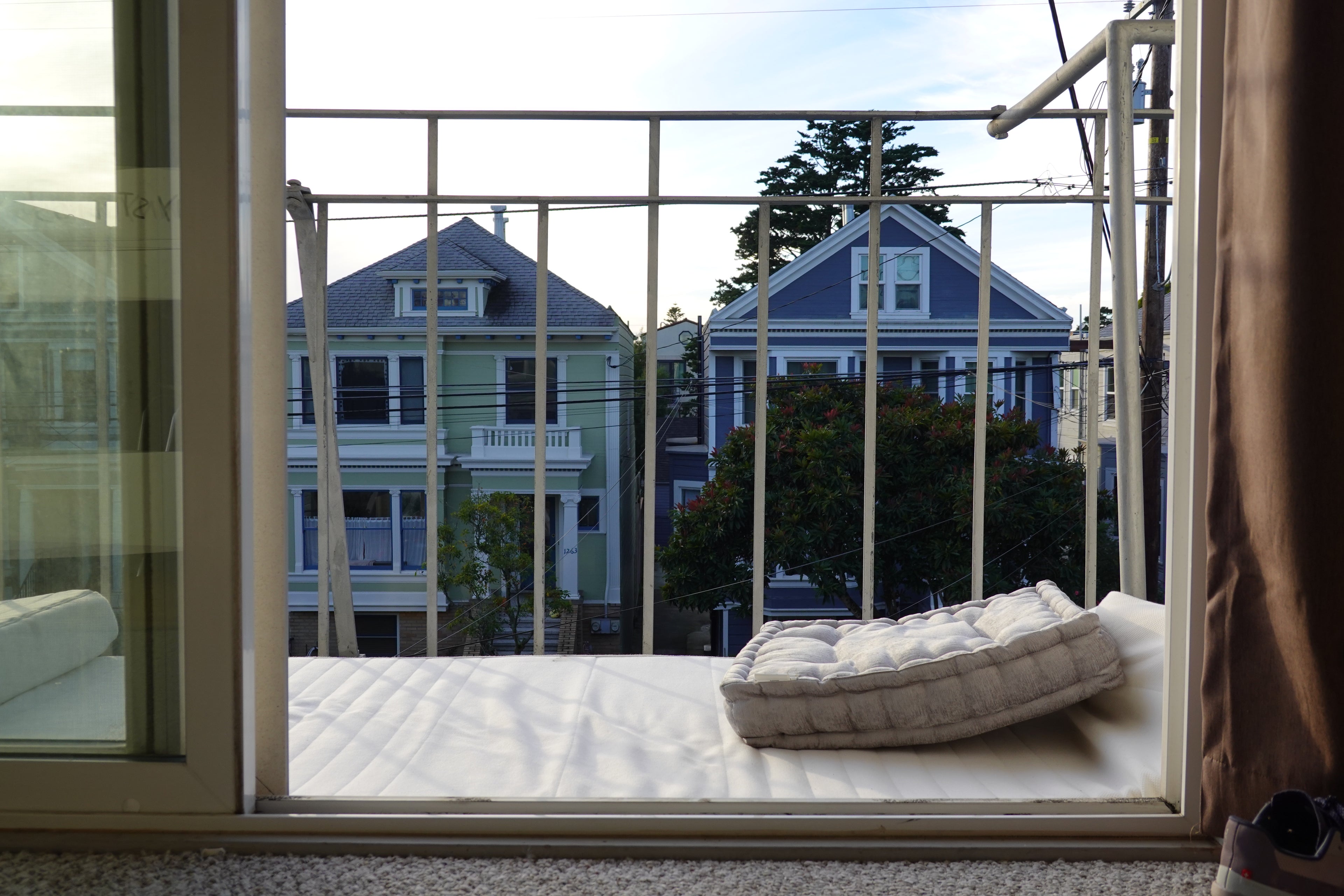 Balcony with a view of houses and trees, featuring a cushioned bench.